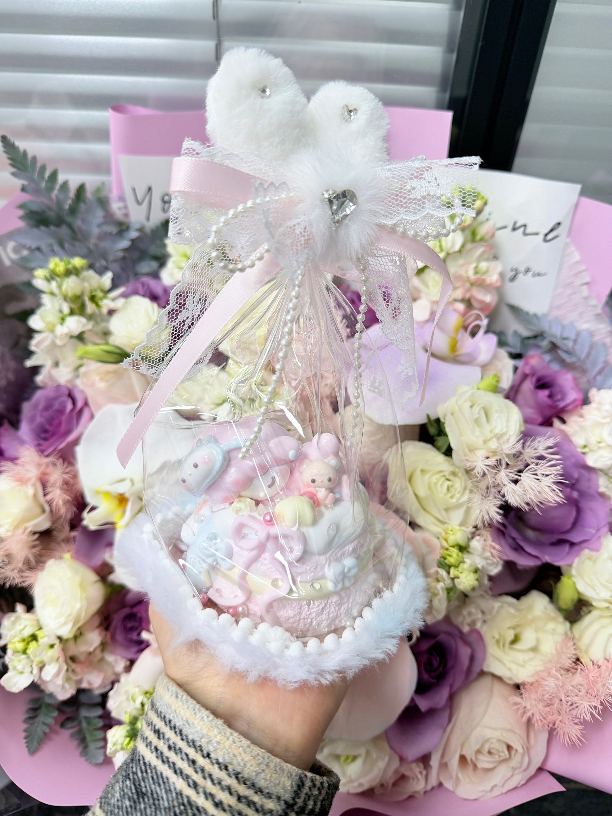 Kawaii cupcake squeeze toy with pink and white whipped cream swirl texture, 3D mini bunny toppers, and pearl bead base, packaged in a clear dome gift bag with fluffy white pompom bow