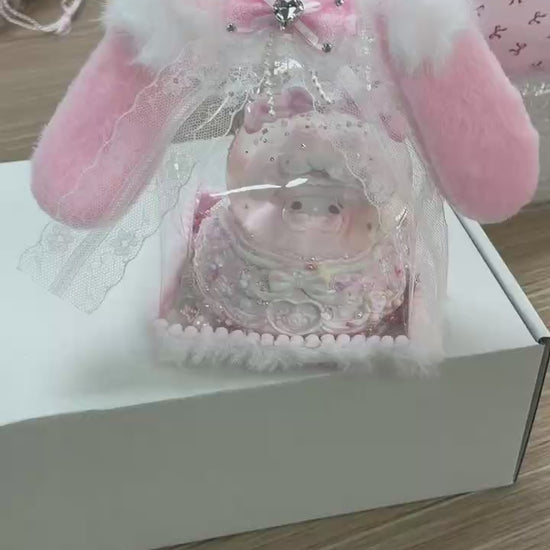 Close-up of food-grade silicone baby pig squishy with pacifier, layered whipped cream body, lace trim, glitter sequins, colourful candy bead decorations, stacked bows, and pearl bead base ring